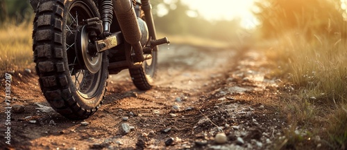 A rugged motorcycle kicks up a cloud of dust as it tears through the grassy field, its tire treads gripping the soil with determination on the rough dirt road