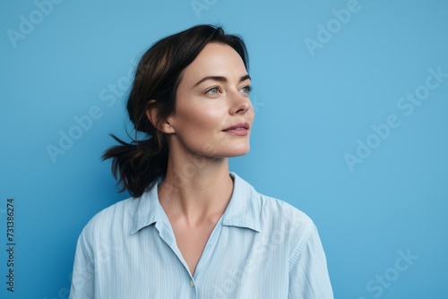Portrait of a beautiful middle aged woman smiling and looking away against blue background