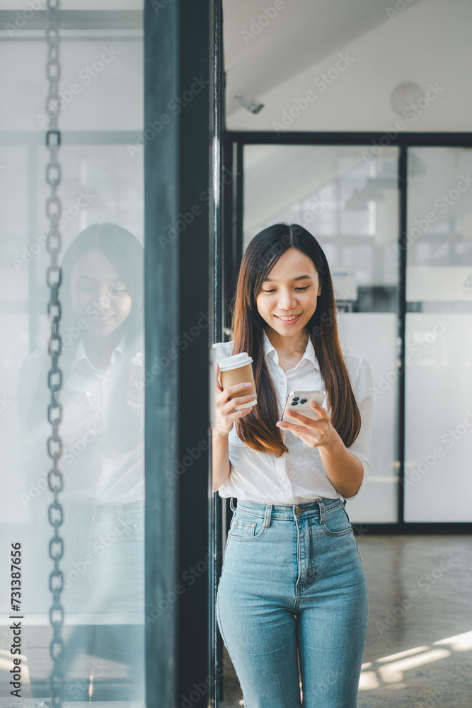 Business technology concept, Young businesswoman with a smartphone enjoying a coffee break in a well-lit office corridor, reflecting on glass. Business technology concept, Young businesswoman with a smartphone enjoying a coffee break in a well-lit office corridor, reflecting on glass.