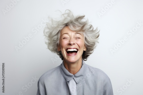 Portrait of happy senior woman laughing and looking at camera over grey background