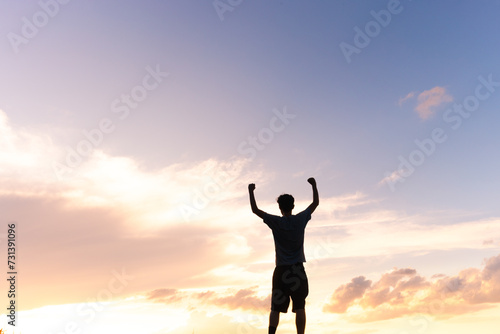 A silhouette of a man against the golden sunset sky, arms raised and fists clenched in a powerful display of determination and strength. Person feeling strong and motivated.