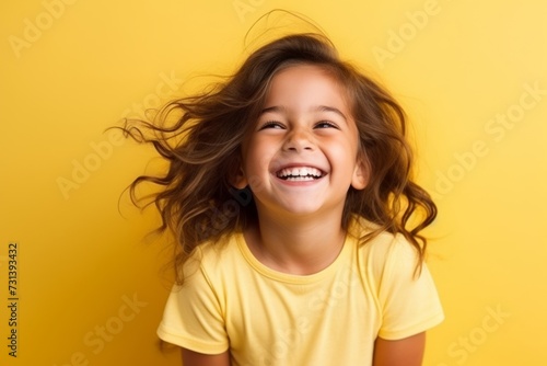 Portrait of a happy smiling little girl with flying hair over yellow background © Inigo