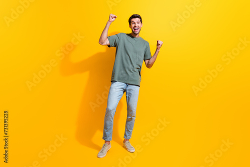 Full length photo of confident lucky guy wear khaki t-shirt rising fists screaming yeah isolated yellow color background