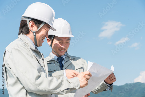 青空で設計図を見る作業服を着た作業員（建設・建築・設計・不動産・土木・工事・現場監督）
 photo