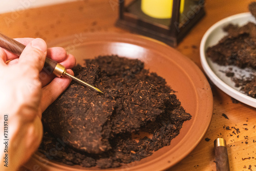 Preparing pu-erh tea: hands using a tea knife to break up pressed tea leaves photo