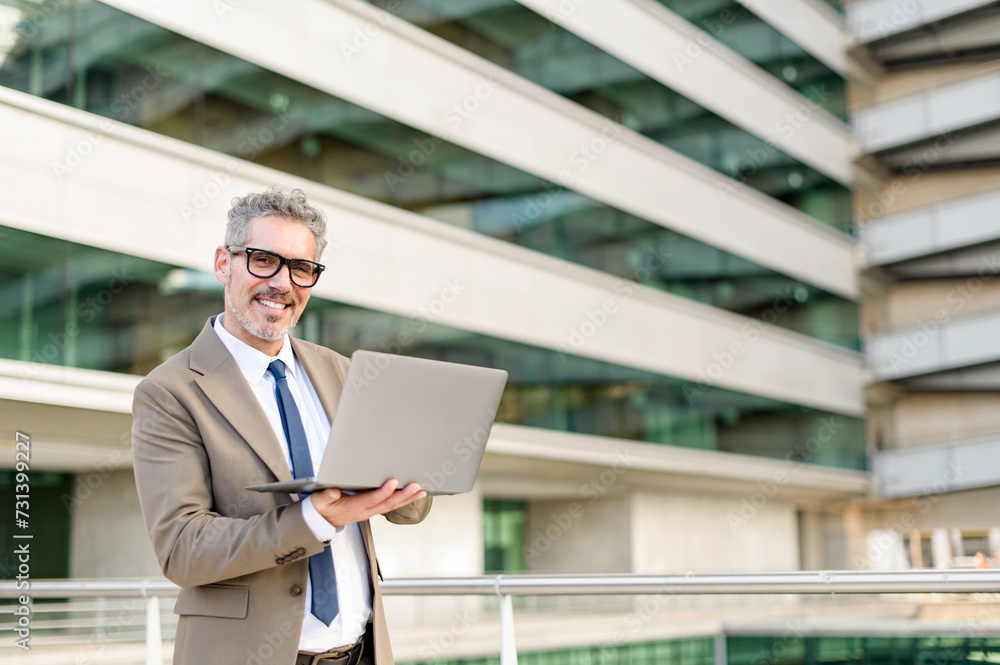 A confident senior 60s businessman in a brown suit stands outdoors, holding his laptop with an engaging smile, showcasing a fusion of experience and modern technology A confident senior 60s businessman in a brown suit stands outdoors, holding his laptop with an engaging smile, showcasing a fusion of experience and modern technology