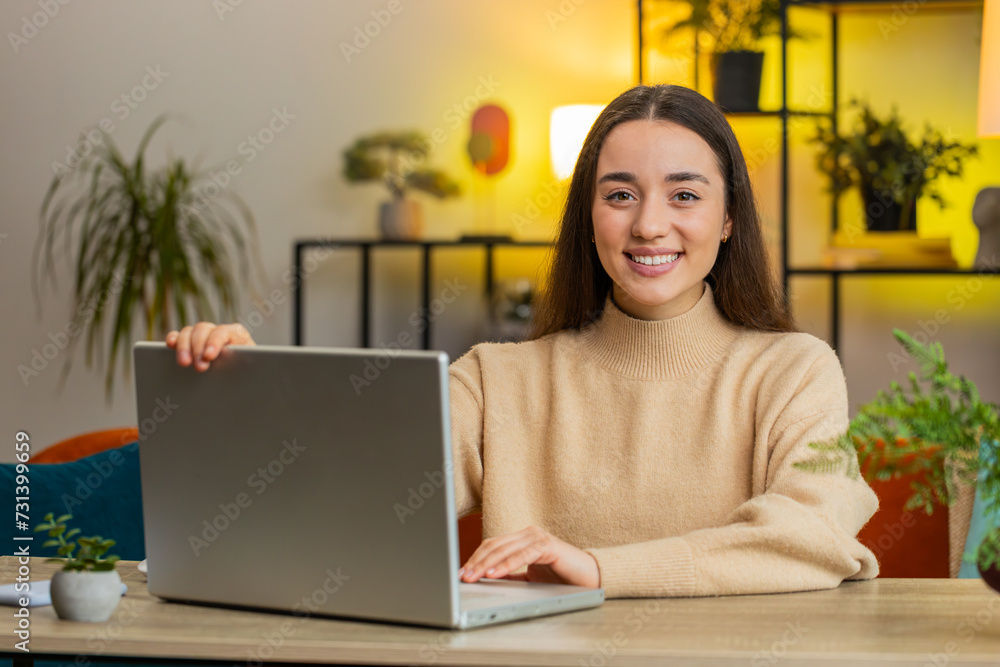 Happy smiling Caucasian young woman freelancer opens laptop working on notebook, sends messages business email makes online purchases watching movies. Female girl sitting at home office room at table Happy smiling Caucasian young woman freelancer opens laptop working on notebook, sends messages business email makes online purchases watching movies. Female girl sitting at home office room at table
