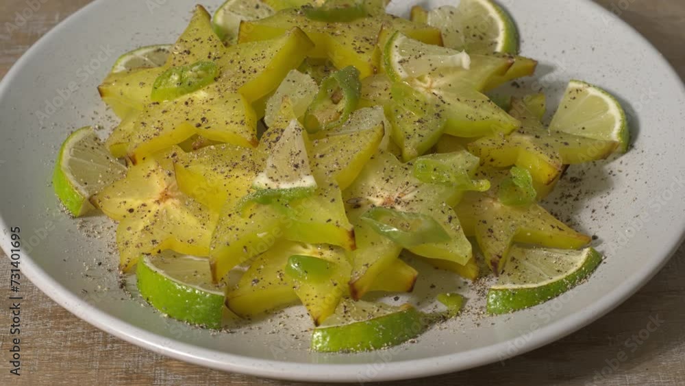 Rotating plate with carambola or star fruit spicy salad with frozen green chili, lime pieces, lime juice, and a lot of black pepper. Perfect condiment for grilled fish or a curry. 