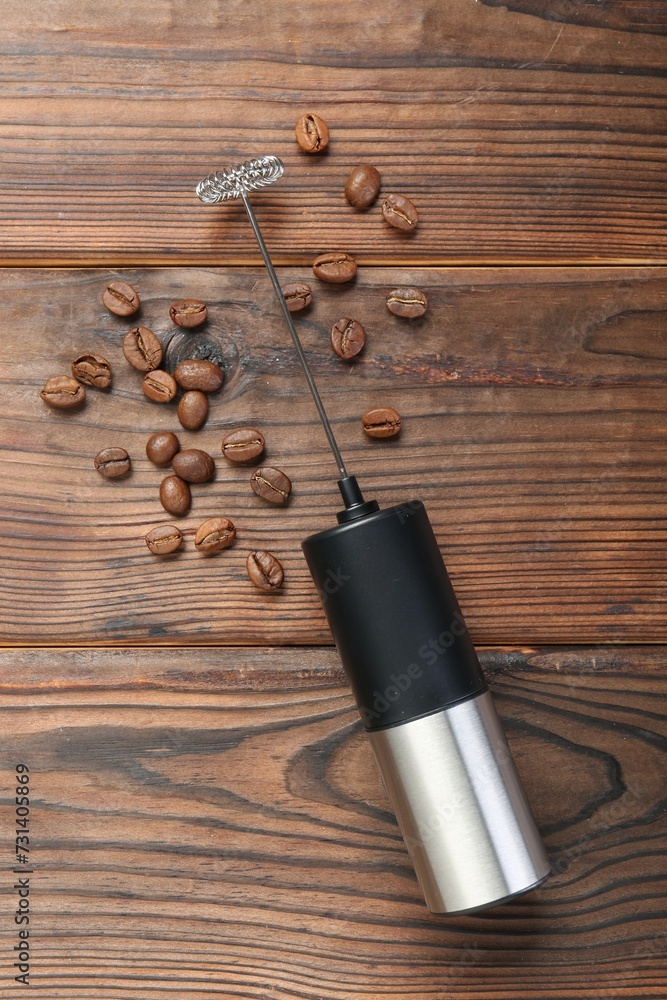 Black milk frother wand and coffee beans on wooden table, top view