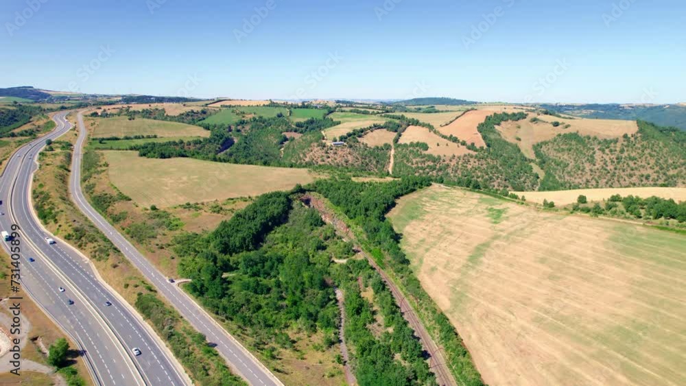 Aerial View Of Cars Driving Through The Road Along The Rural Fields And Hills In Aveyron, France. Aerial View Of Cars Driving Through The Road Along The Rural Fields And Hills In Aveyron, France.