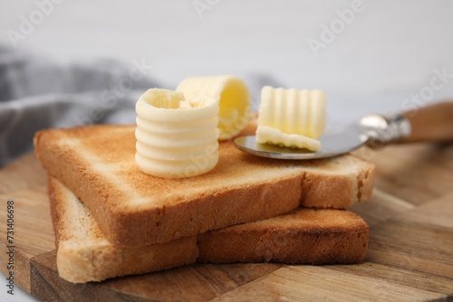 Tasty butter curls, knife and toasts on wooden board, closeup