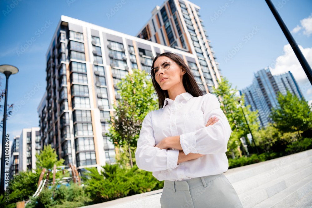 Photo of gorgeous lovely lady standing with folded arms in sunny city business center modern buildings Photo of gorgeous lovely lady standing with folded arms in sunny city business center modern buildings
