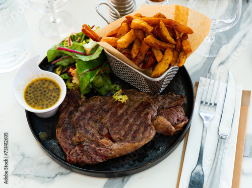 Fotografia Juicy beef entrecote served with French fries, fresh greens salad and piquant lemon mustard sauce with capers