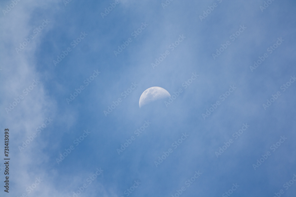beautiful half moon in the day surrounded by wispy clouds in a blue sky beautiful half moon in the day surrounded by wispy clouds in a blue sky