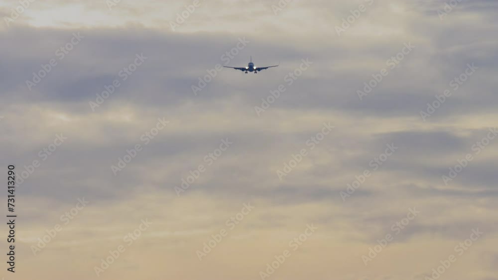 Jet plane approaching landing. Passenger airliner flies in the cloudy sunset sky, front view, long shot. Cinematic footage of aviation. Background crimson sky Jet plane approaching landing. Passenger airliner flies in the cloudy sunset sky, front view, long shot. Cinematic footage of aviation. Background crimson sky