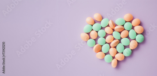 An array of pastel peach and mint green pills arranged in a heart shape on a lavender background. Place for text © evgenia_lo
