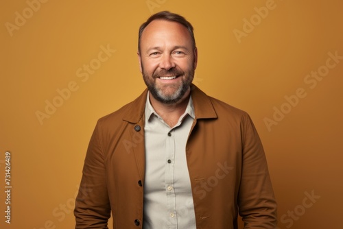 Portrait of happy mature man smiling and looking at camera while standing against yellow background