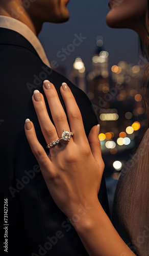Woman's hand with an engagement ring embracing a man, with a cityscape in the background at night.