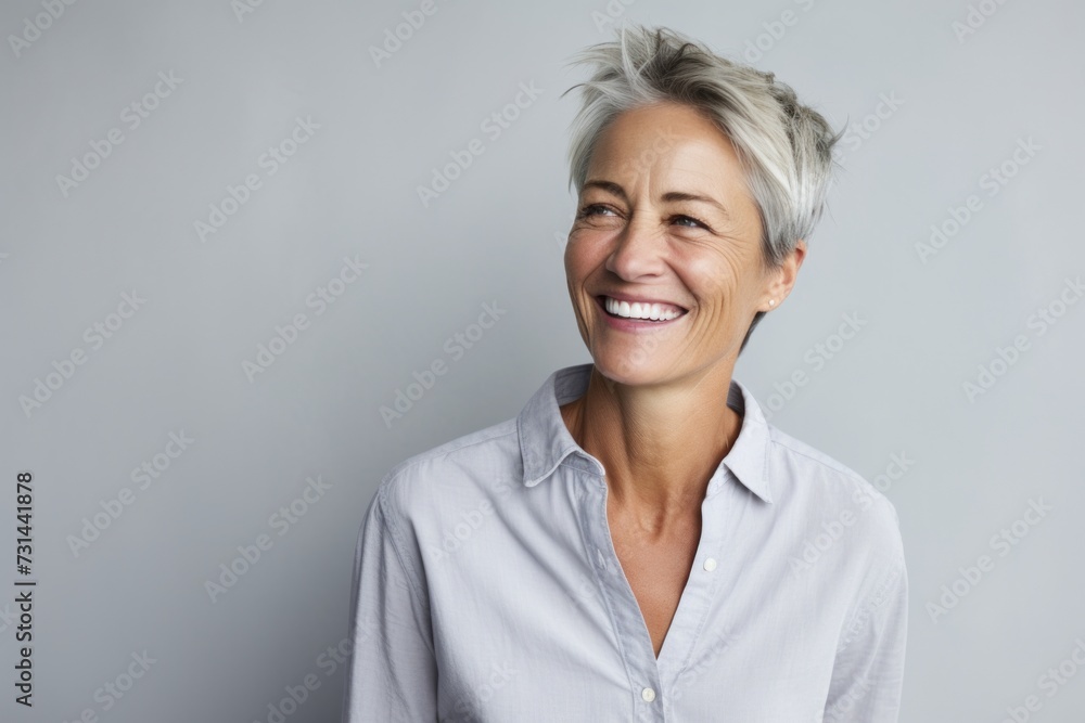 Portrait of a happy senior woman smiling at the camera while standing against grey background Portrait of a happy senior woman smiling at the camera while standing against grey background