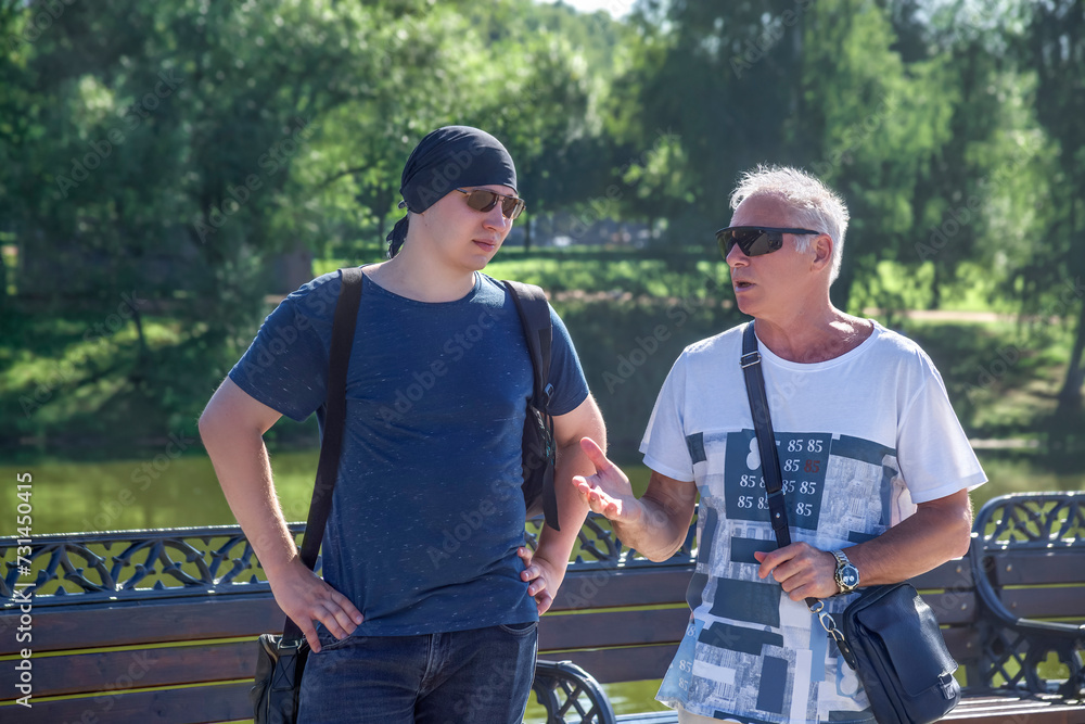 Men of two generations in informal clothes are having a conversation in a city park on a summer day Men of two generations in informal clothes are having a conversation in a city park on a summer day