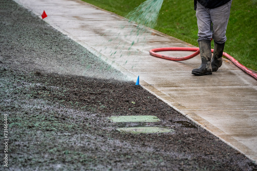 Professional hydroseeding, workman spraying a mix of grass seed and wood pulp from a big hose onto a freshly prepared dirt in a new residential community
 photo