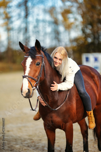 Young blonde girl with her brown horse on the riding arena in portraits.