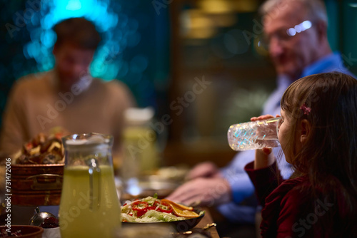 In a modern restaurant, a young girl participates in iftar by breaking her fast with water, embodying the tradition and significance of Ramadan in a contemporary setting.