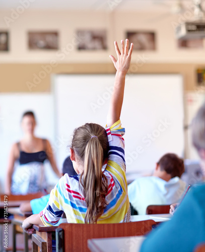 Question, student and hand raised for knowledge in classroom, solution and girl at school. Female person, back and curious for answer or information, learning and studying or education for growth photo