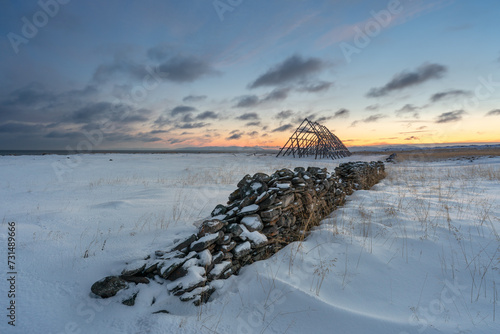 An old stone fence and a fish drying rack at the coast of the Varanagerfjord on a cold winter day during the polar night, Ekkerøya, Northern Norway photo