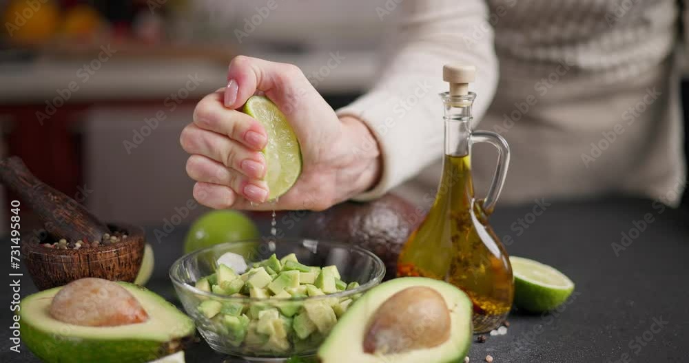 Woman squeezes fresh lime juice onto Chopped avocado in glass bowl at domestic kitchen Woman squeezes fresh lime juice onto Chopped avocado in glass bowl at domestic kitchen