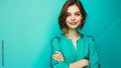 Smiling girl with a chic haircut wearing a bright turquoise blouse, her hands gently crossed, posed against a uniform blue background, in high resolution