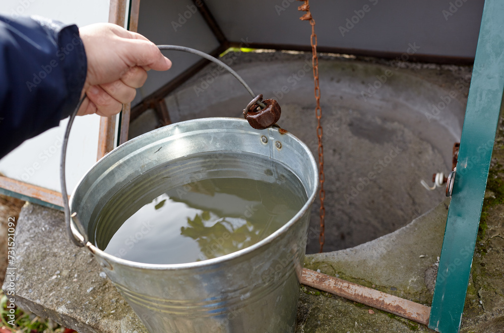 Man hand holding metal bucket with fresh water. Water from a deep well in rural area Man hand holding metal bucket with fresh water. Water from a deep well in rural area