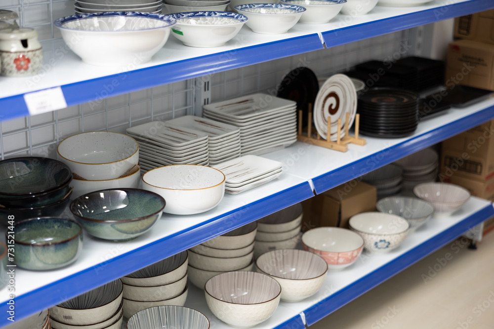 There is assortment of kitchen utensils on supermarket shelf. In cookware department, ceramic plates of various shapes and sizes, with different patterns, are on shelves