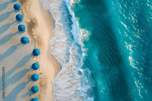 Aerial drone shot of a sandy beach with turquoise seawater and vibrant blue umbrellas