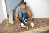 Adult man installing laminate panel on substrate with technology using soft hammer while working in apartment