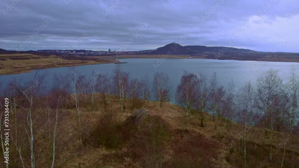 Establishing aerial drone shot of anthropogenic Lake Most (Jezero Most) with town and Hnevin castle in background. Cloudy overcast day. Recultivation of surface brown coal mines to recreational area. Establishing aerial drone shot of anthropogenic Lake Most (Jezero Most) with town and Hnevin castle in background. Cloudy overcast day. Recultivation of surface brown coal mines to recreational area.