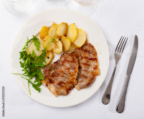 Delicious fried pork with potatoes and fresh arugula served on platter