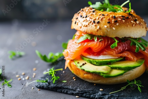 Freshly baked bagel topped with smoked salmon avocado and egg Served on a slate table photo
