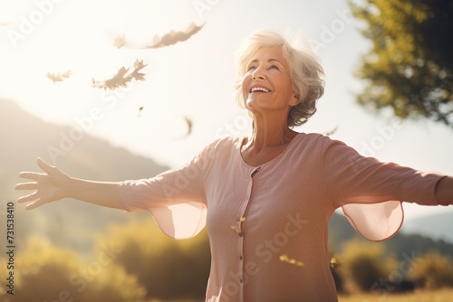 An elderly happy woman stands facing the camera against the background of nature, the sea, with her arms outstretched. Relaxation and happiness in harmony with yourself