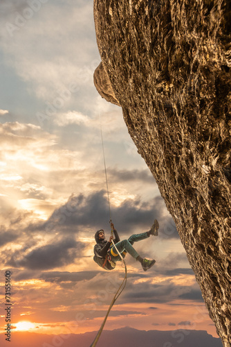 Person climbing, rappelling on mountain at sunset with golden light, sky with clouds, oranges