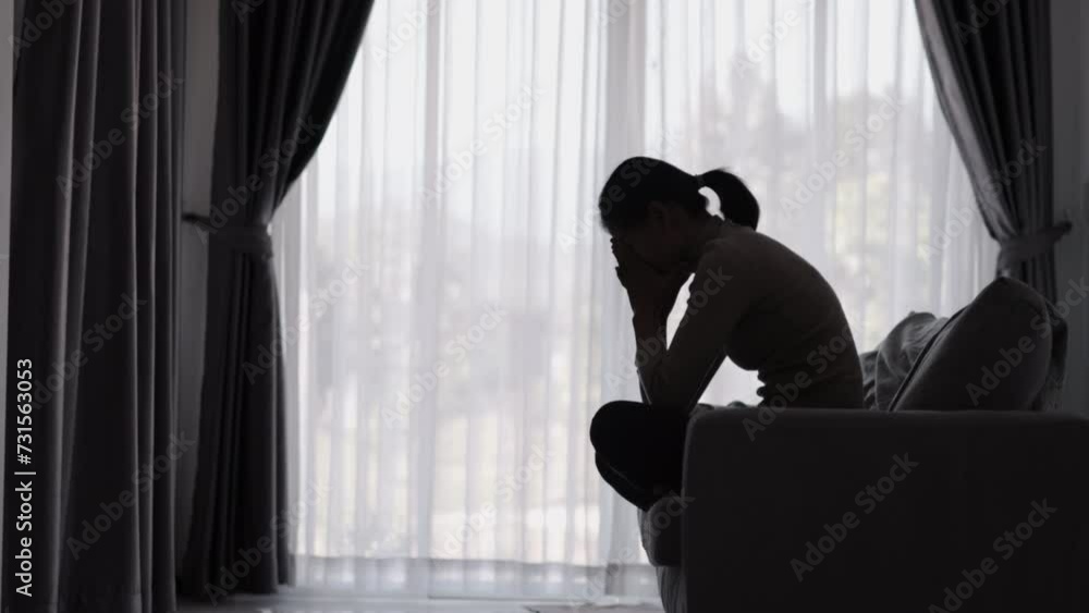 Silhouette of a person suffering from depression in the house, Depressed woman sitting alone on the Sofa feel stress, sad and worried in the dark room. person are stressed. Silhouette of a person suffering from depression in the house, Depressed woman sitting alone on the Sofa feel stress, sad and worried in the dark room. person are stressed.