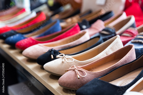 Row of ballet shoes displaced on shelf in shoe store.