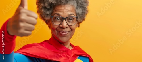 A happy elderly woman in a superhero costume, wearing glasses and a smile, gives a thumbs up gesture, promoting vision care and eyewear.
