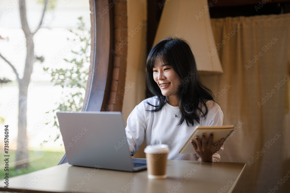 Cheerful young woman with a laptop and notebook, enjoying her work from home setup in a sunny room.. Cheerful young woman with a laptop and notebook, enjoying her work from home setup in a sunny room..