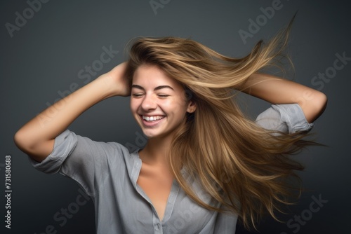 studio shot of a happy young woman holding her hair and posing against a grey background