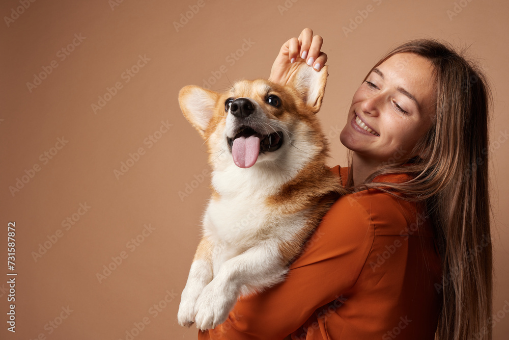 Girl hugging Pembroke Welsh Corgi on a beige clean background in the studio, love for animals Girl hugging Pembroke Welsh Corgi on a beige clean background in the studio, love for animals