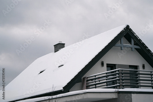 The roof of the family house in winter. Winter landscape with falling snow and the smoke from a chimney heating a home during the chilly season. © AlexGo