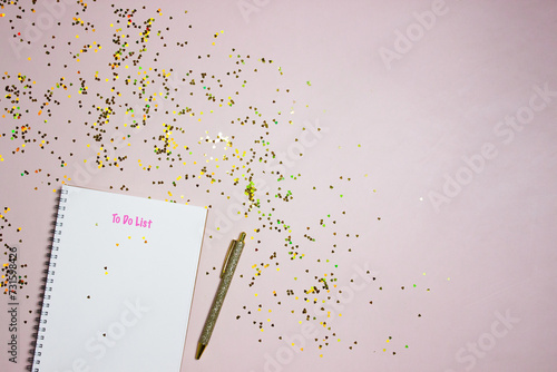 To do list concept with a white notebook, golden pen and glitter over the pink background. 