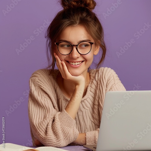Cheerful young woman with glasses and a beaming smile, comfortably working on a laptop, against a soft purple background.