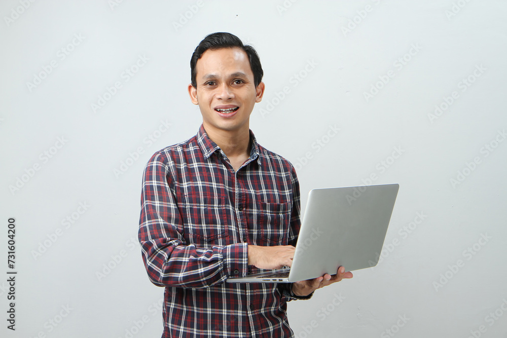 Happy asian indonesian man holding laptop computer on isolated background Happy asian indonesian man holding laptop computer on isolated background